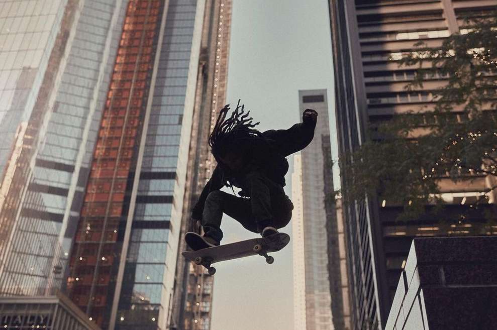 A skateboarder performs a trick mid-air in an urban setting, with tall buildings in the background, showcasing urban lifestyle and sports.