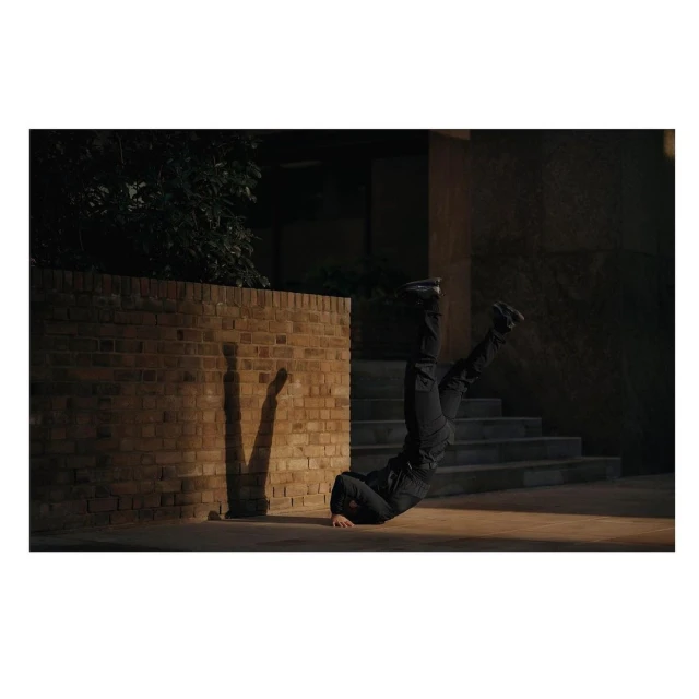 Adult performs a headstand outside against a brick wall at night with a shadow cast on the brick surface.