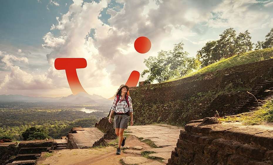 Woman with a backpack hikes up a stone path on a sunny day with a bright sky. A large red brand logo is superimposed on the image.