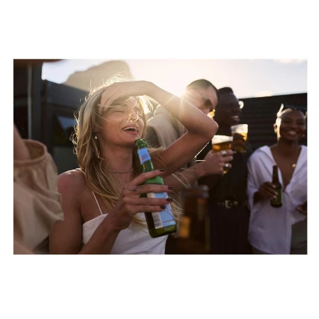 A group of diverse young adults are enjoying an outdoor gathering at sunset, drinking beer and laughing together in a social setting.