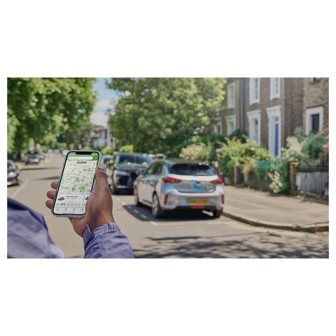 Person holds smartphone with map app on the street, with parked cars and buildings in the background, photographed on a sunny day.