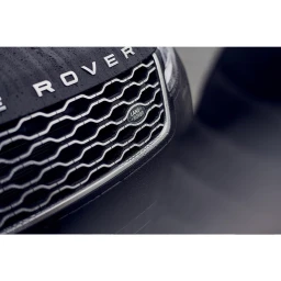 Close-up detail of a dark Range Rover front grille and hood with water droplets under soft lighting.