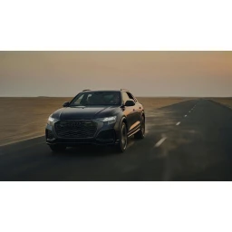 A dark SUV driving along a straight desert road during sunset, photographed by Matthew Joseph in London.