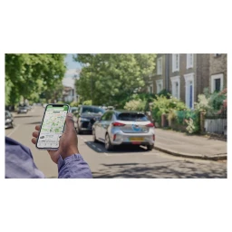 Person holding a smartphone displaying a map application while standing on a residential street with parked cars
