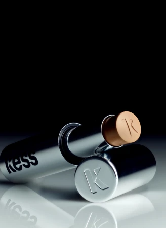 Silver cosmetic stick with embossed lettering and a tan cap resting on a reflective surface against a dark background