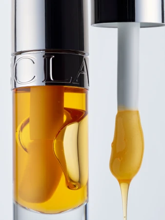 Close-up product shot of a clear cosmetic bottle with golden serum and a dropper dripping amber liquid against a white background