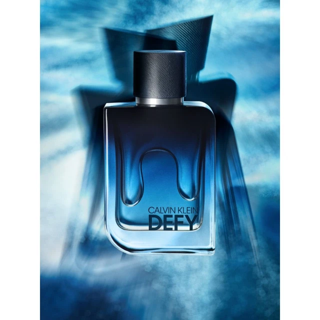 Calvin Klein Defy fragrance bottle with blue gradient fill stands against a blue hazy background, clean product shot for beauty.