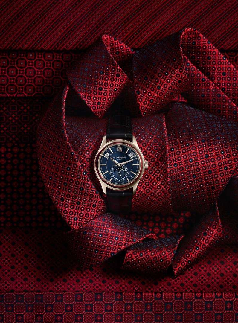 Elegant gold wristwatch with a navy blue face displayed on a patterned red fabric, showcasing luxury timepiece craftsmanship and design.