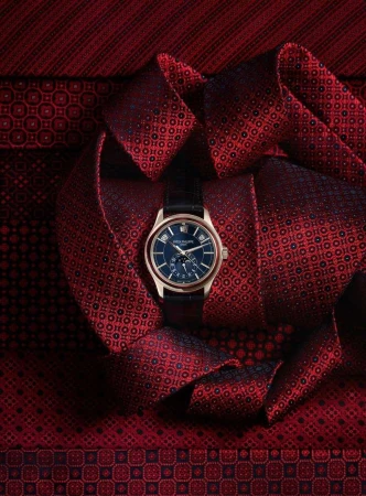Elegant gold wristwatch with a navy blue face displayed on a patterned red fabric, showcasing luxury timepiece craftsmanship and design.
