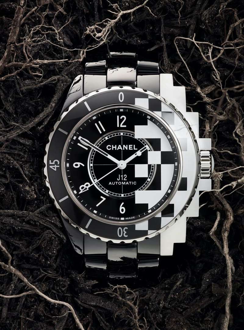 Luxury Chanel J12 watch on dark textured background with black and white checkerboard dial and stainless steel bracelet.