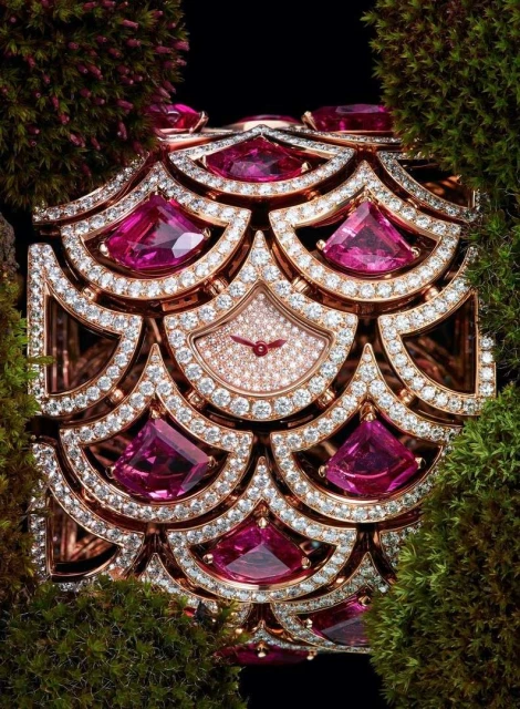 Ornate rose gold wristwatch with diamonds and rubies, set among green moss against a black backdrop in a studio setting.