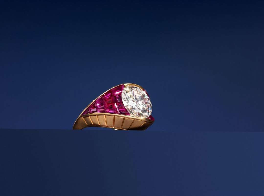 Gold ring featuring a large diamond encircled by rubies on a dark blue surface, showcasing fine jewelry craftsmanship and design.