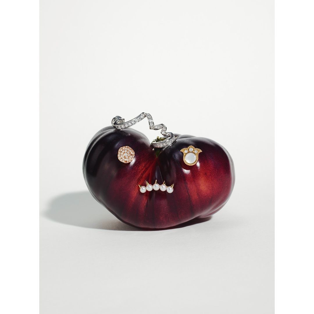 Dark red heirloom tomato with gold and pearl jewelry on a white background for a high fashion food still life shot.