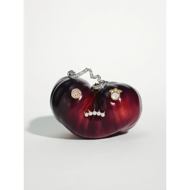 Dark red heirloom tomato with gold and pearl jewelry on a white background for a high fashion food still life shot.