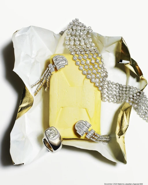 Elevated still life shot of a diamond ring, diamond necklace, and earrings presented on rumpled gold and white paper.