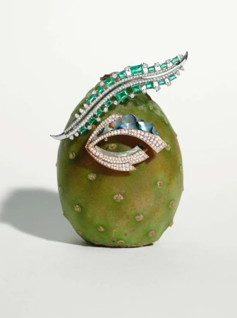 Still life photograph of a prickly pear fruit with two jeweled brooches attached against a stark white background. High-end jewelry.