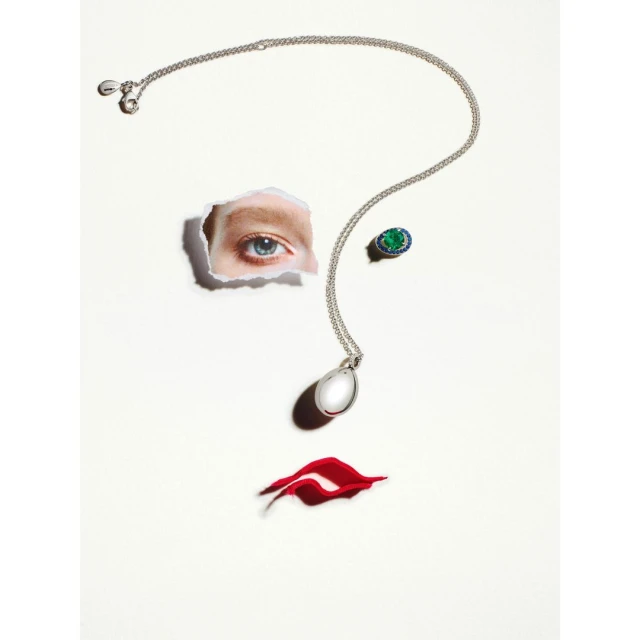 Creative fashion still life with a necklace, ring, and red paper lips forming a woman's face on a white background.