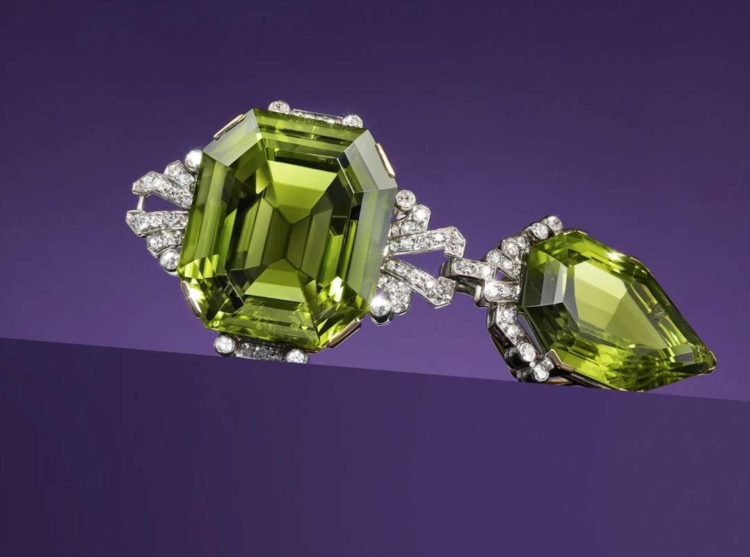 Close-up of a vintage-inspired brooch featuring a large, emerald-cut peridot gemstone with smaller diamonds, against a purple backdrop.