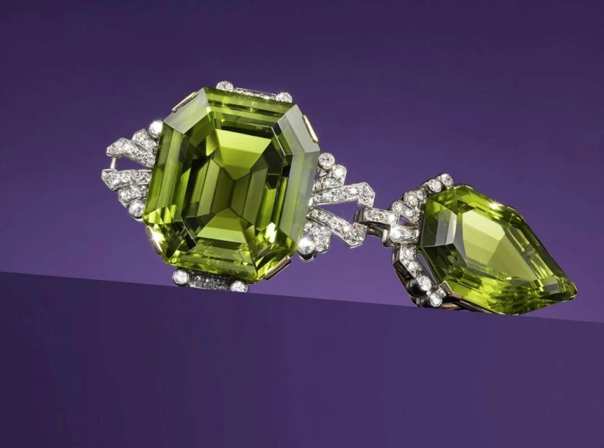 Close-up of a vintage-inspired brooch featuring a large, emerald-cut peridot gemstone with smaller diamonds, against a purple backdrop.