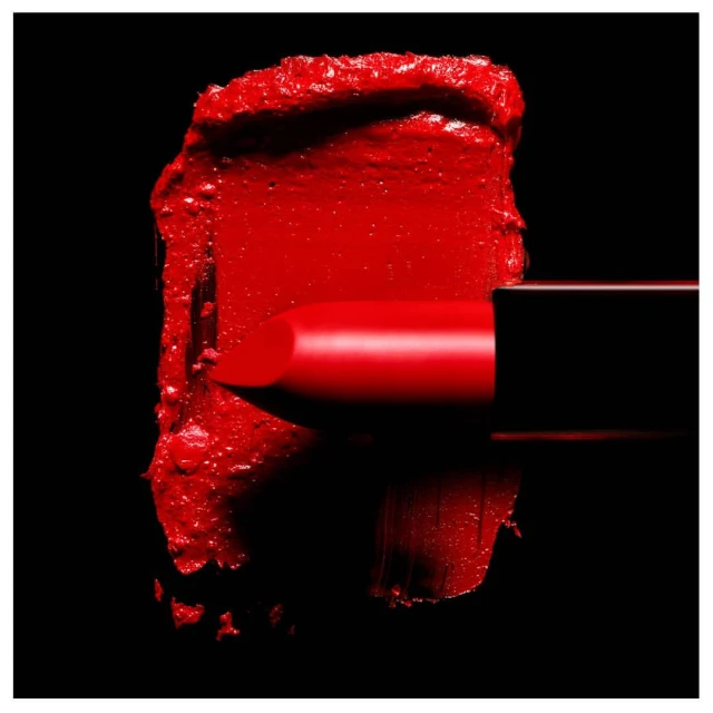 Macro shot of a vibrant red lipstick bullet partially inserted into a matching smear of lipstick against a stark black background.