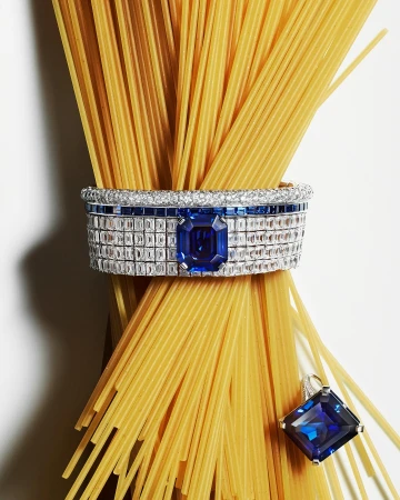 Still life shot of uncooked spaghetti tied with a diamond and sapphire bracelet and matching pendant on a white background.