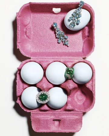 Overhead studio shot: gemstones and jewelry on white eggs inside a pink egg carton, creating an eye-catching, colorful composition.