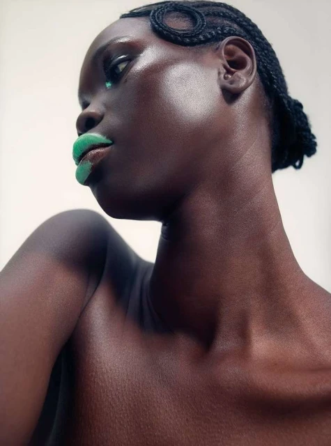 Striking portrait of a Black woman with intricate braided hairstyle and glossy green lipstick against a clean, neutral backdrop in studio lighting.