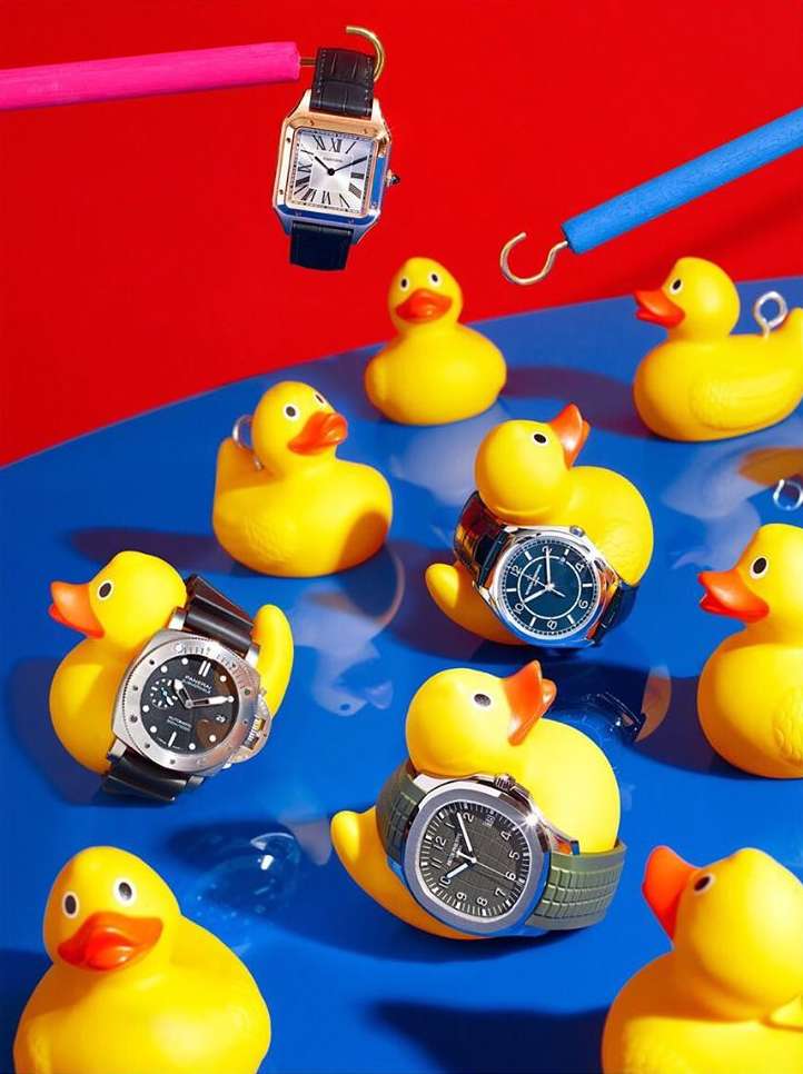 Still life arrangement: Yellow rubber ducks wearing wristwatches float on blue with red background, creating playful contrast.