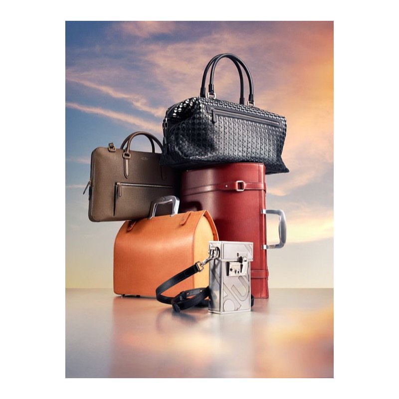 Stacked leather bags and luggage in warm neutral tones against a soft sunset sky background, studio shot, product photography.