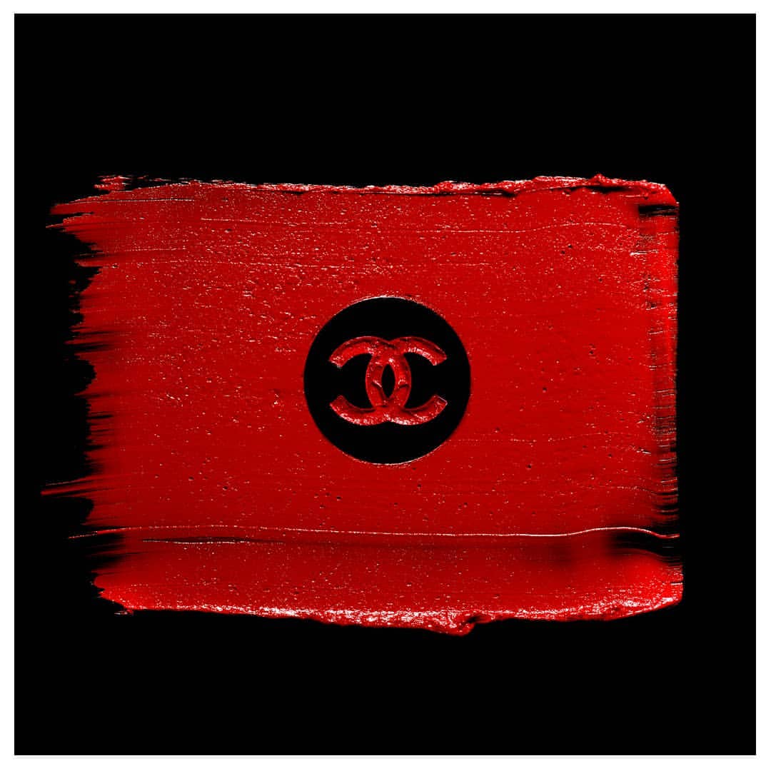 Close-up of red lipstick smear with Chanel logo imprint against a black background, emphasizing luxury cosmetics.