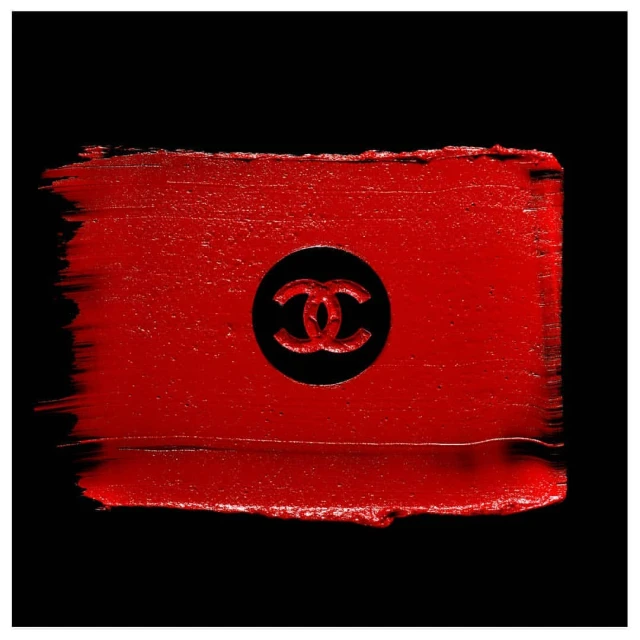 Close-up of red lipstick smear with Chanel logo imprint against a black background, emphasizing luxury cosmetics.