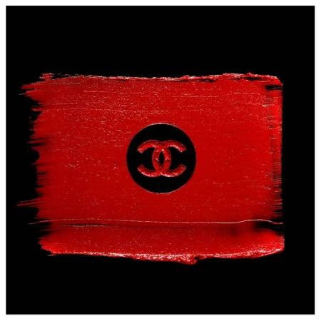 Close-up of red lipstick smear with Chanel logo imprint against a black background, emphasizing luxury cosmetics.