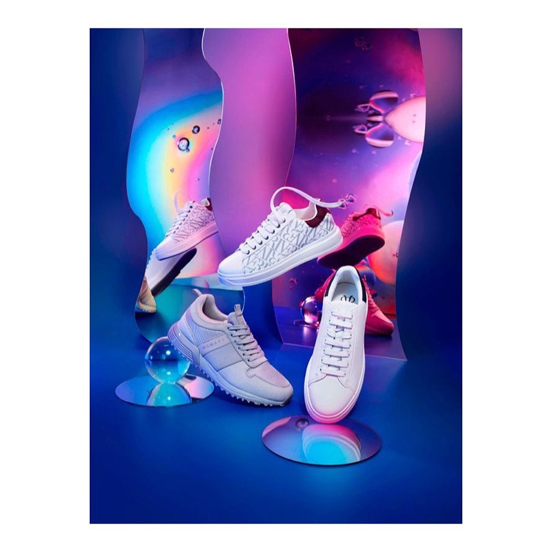 Fashion still life featuring multiple white sneakers in a colourful studio setting with mirrored surfaces and abstract background elements.
