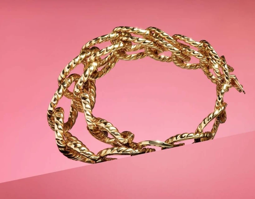 Golden chain bracelet is displayed against a pink backdrop in a product shot that highlights the bracelet's intricate links and texture.