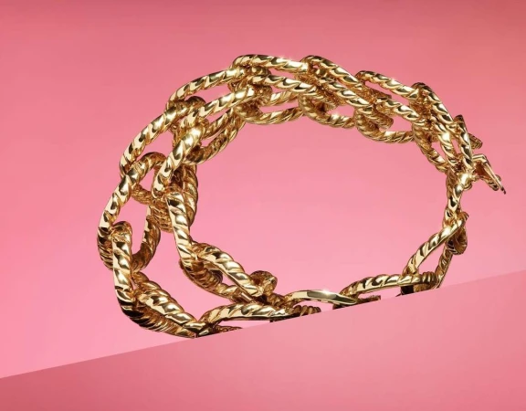 Golden chain bracelet is displayed against a pink backdrop in a product shot that highlights the bracelet's intricate links and texture.