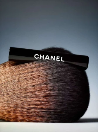 Chanel brand make-up brush with black handle and soft brown bristles on gradient grey background in beauty product photography.