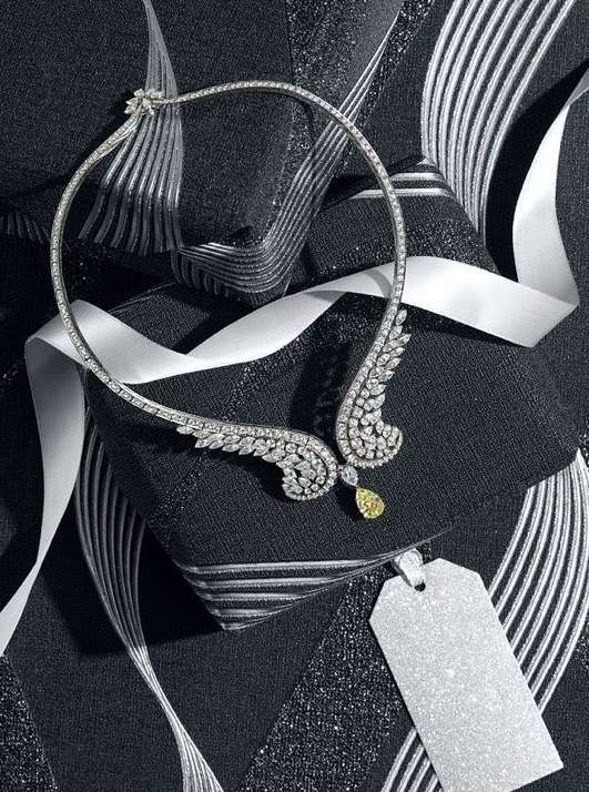 Elegant diamond necklace featuring a yellow teardrop gemstone, displayed on a textured black surface with white ribbons and a price tag.