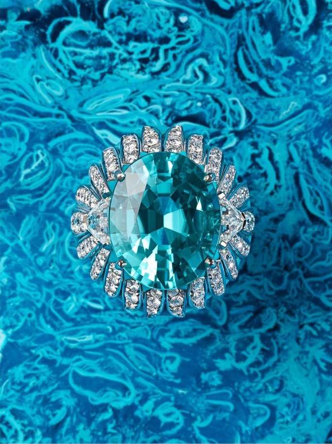 Close-up studio shot of an oval aquamarine cocktail ring with diamond accents set against a swirling turquoise backdrop.
