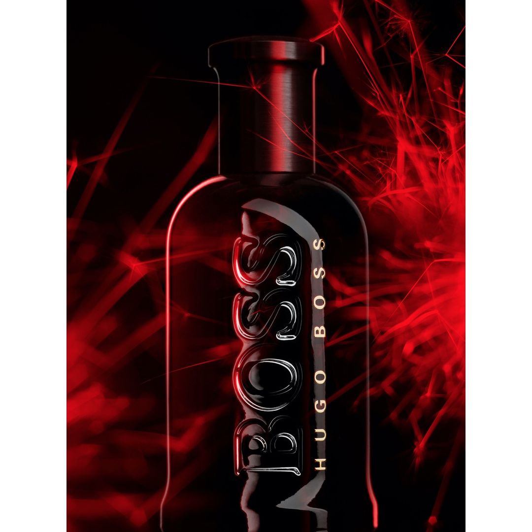 A sleek, black Hugo Boss perfume bottle with prominent branding stands against a dark background illuminated by red light streaks.