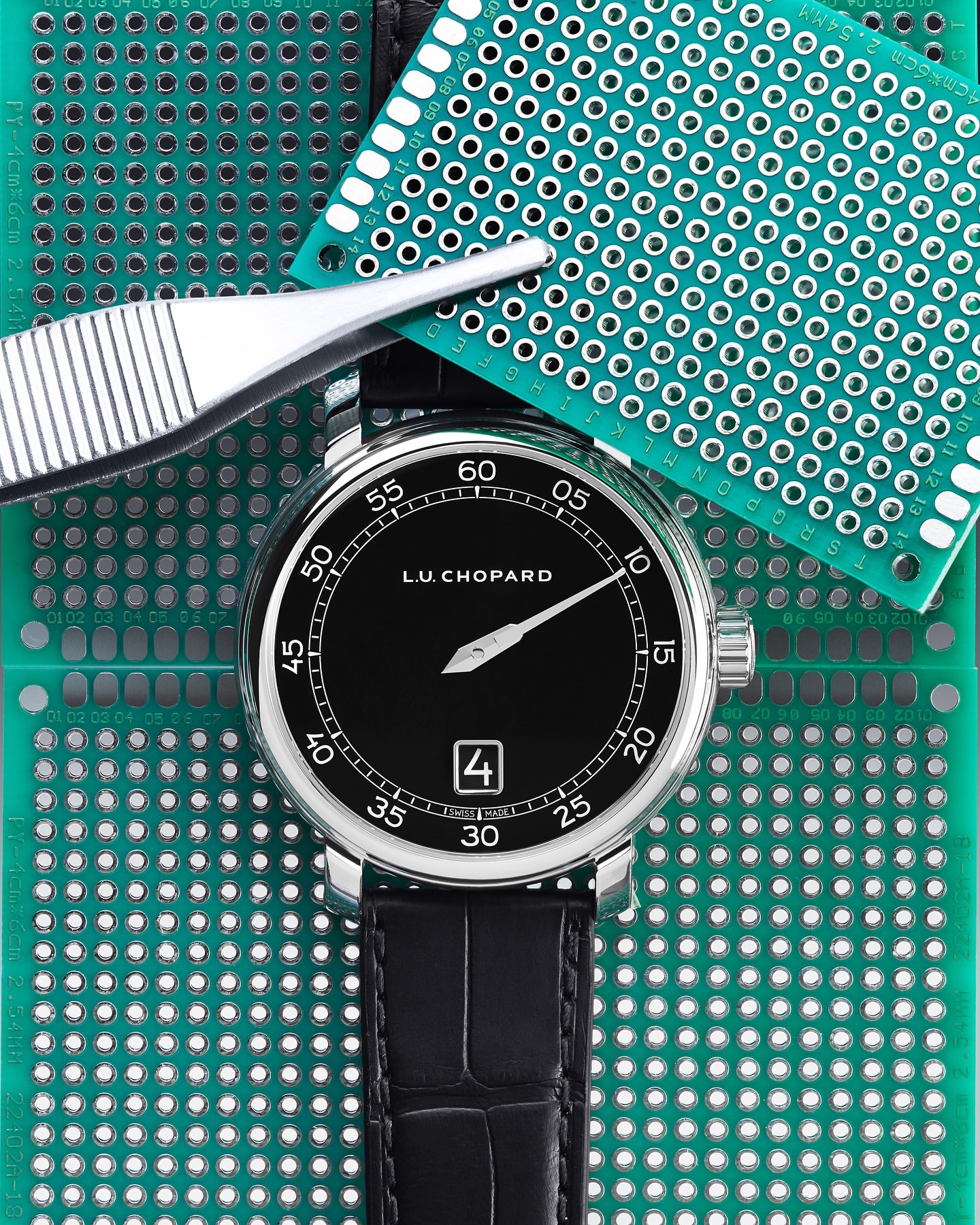 Close-up of a luxury wristwatch on a green circuit board, complemented by precision tweezers for detailed technology or craftsmanship.