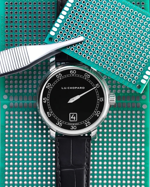 Close-up of a luxury wristwatch on a green circuit board, complemented by precision tweezers for detailed technology or craftsmanship.