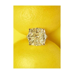 Cushion cut yellow diamond ring positioned between two whole yellow citrus fruits against a bright yellow backdrop.