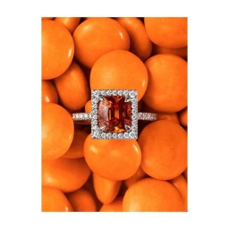 Close-up macro shot of a square orange gemstone ring resting on a pile of round orange candies.