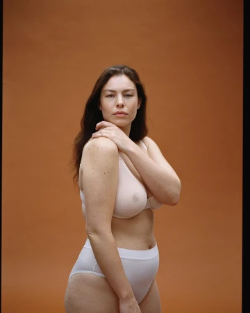 Woman with long dark hair wearing white lingerie against a solid brown background, photographed by Matthew Sprout.