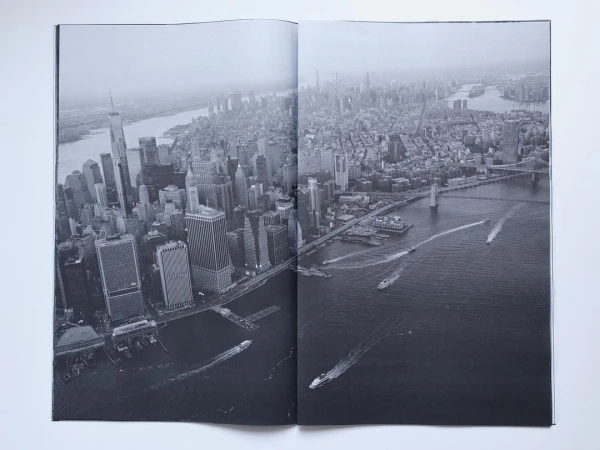 High-angle black and white photograph shows New York City skyline with tall buildings, waterways, and boat traffic.