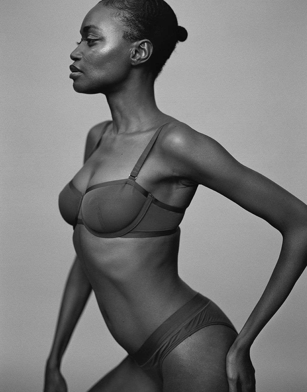 Monochrome portrait of an African woman posing in a bra and underwear against a gray background, showcasing a minimalist aesthetic.