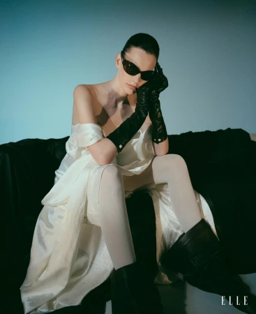 Model in white satin dress wearing black sunglasses, long gloves and boots seated on sofa by Matthew Sprout