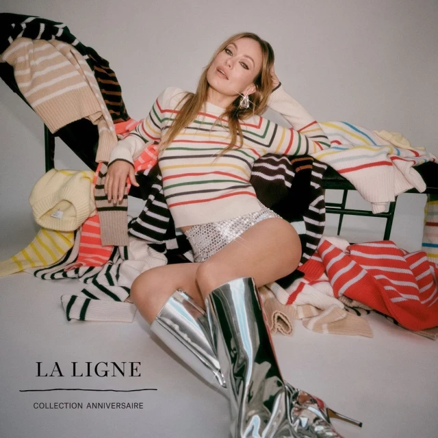 Woman poses in silver boots, striped sweater, and embellished shorts, surrounded by sweaters and the 'LA LIGNE' logo.