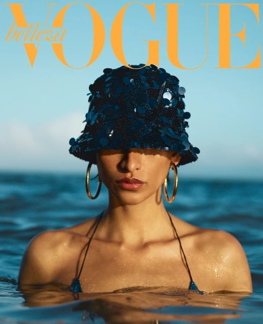 Magazine cover featuring a woman in a sequined hat standing in water with the 'Vogue' logo at the top against a blue sky background.