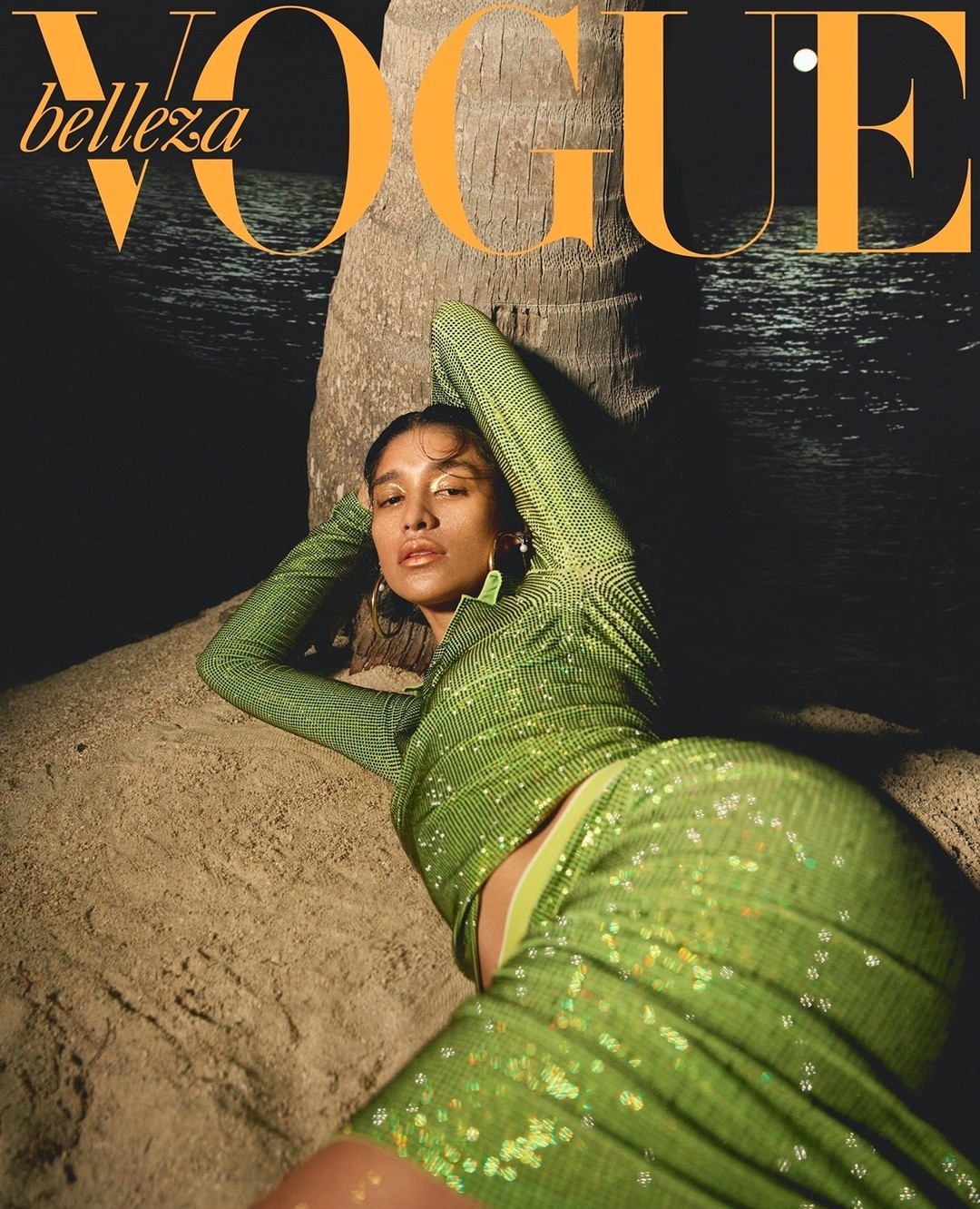 Magazine cover featuring a woman in a green sequin dress reclining against a palm tree at night. Vogue logo visible at the top.